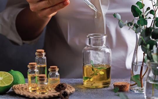 Woman hand pouring eucalyptus essential oil into bottle on grey table