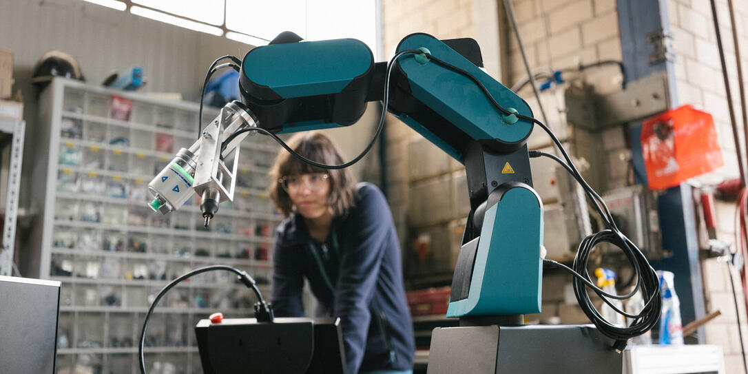 female technician programs a robot arm with a digital tablet