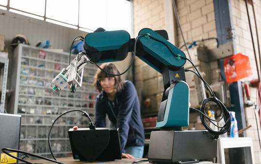 female technician programs a robot arm with a digital tablet