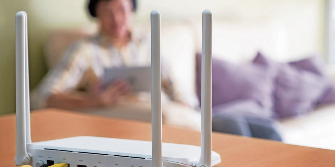 Selective focus at router. Internet router on working table with blurred man using tablet at the background. Fast and high speed internet connection from fiber line with LAN cable connection.