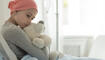 Weak girl with cancer wearing pink headscarf and hugging teddy bear