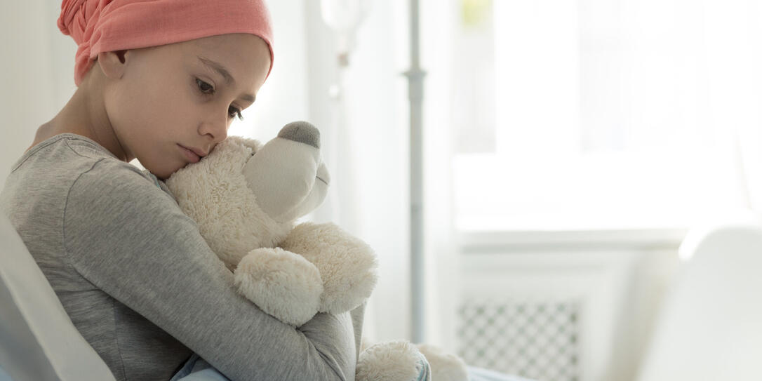 Weak girl with cancer wearing pink headscarf and hugging teddy bear