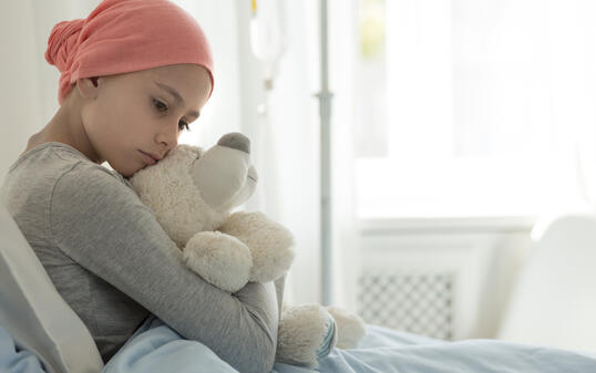 Weak girl with cancer wearing pink headscarf and hugging teddy bear