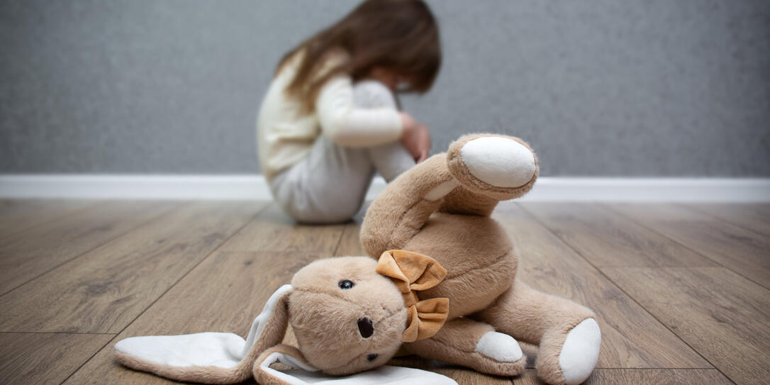 A stuffed bunny on the floor, a scared child sitting behind it. Child abuse. Bullying in the family.