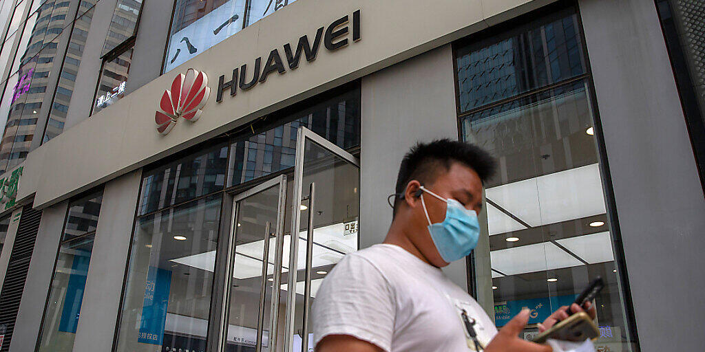 ARCHIV - Ein Mann mit Gesichtsmaske schaut auf sein Smartphone, als er an einem Huawei-Laden in Peking vorbeigeht. Der chinesische Technologiekonzern Huawei soll nun endgültig nicht am Ausbau des superschnellen 5G-Mobilfunknetzes in Großbritannien beteiligt werden. Foto: Mark Schiefelbein/AP/dpa