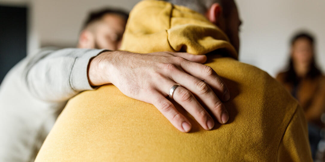 Man embracing his friend who is sharing his story at the group therapy session
