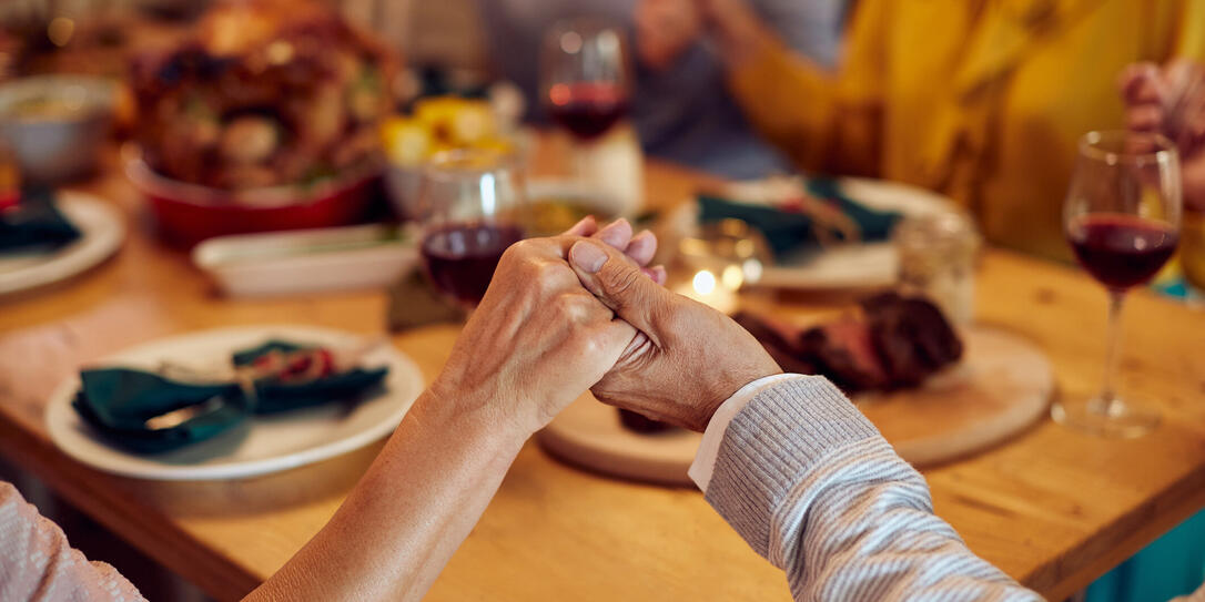 Close-up of senior couple saying grace during Thanksgiving meal with their family.