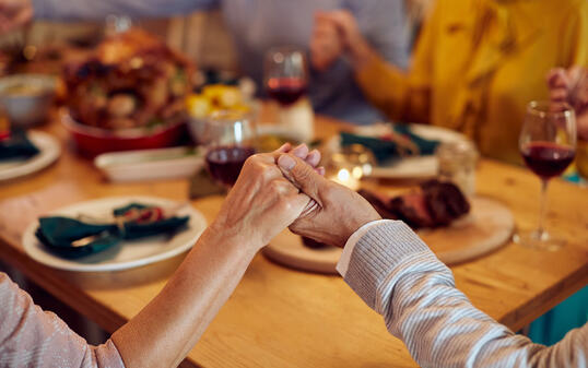 Close-up of senior couple saying grace during Thanksgiving meal with their family.