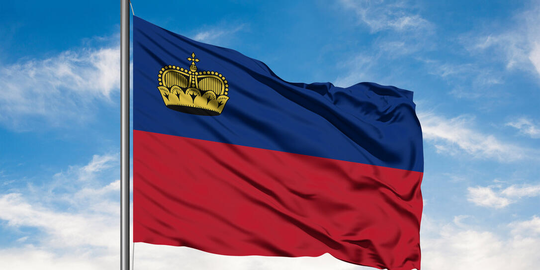 Flag of Liechtenstein waving in the wind against white cloudy blue sky.