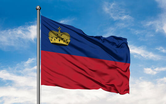 Flag of Liechtenstein waving in the wind against white cloudy blue sky.