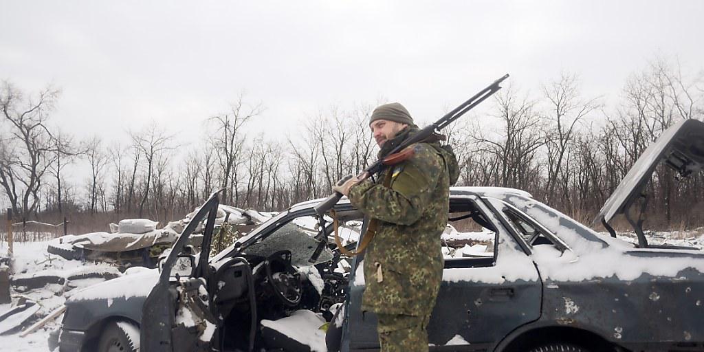 Ein ukrainischer Soldat in der Ostukraine neben einem von den Kämpfen beschädigtem Auto. (Archiv)
