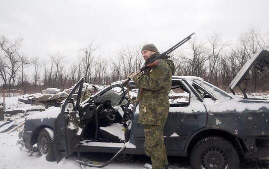 Ein ukrainischer Soldat in der Ostukraine neben einem von den Kämpfen beschädigtem Auto. (Archiv)