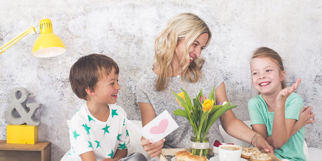 Mother´s Day - two children surprise their mother with breakfast in modern bed