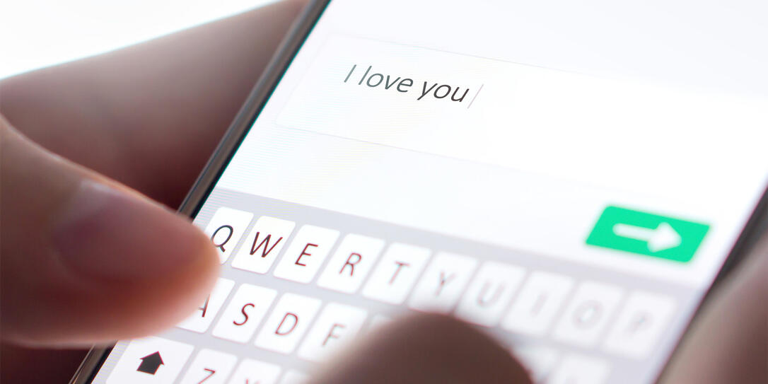 Sending I love you text message with mobile phone. Online dating, texting or catfishing concept. Romance fraud, scam or deceit with smartphone. Man writing comment.