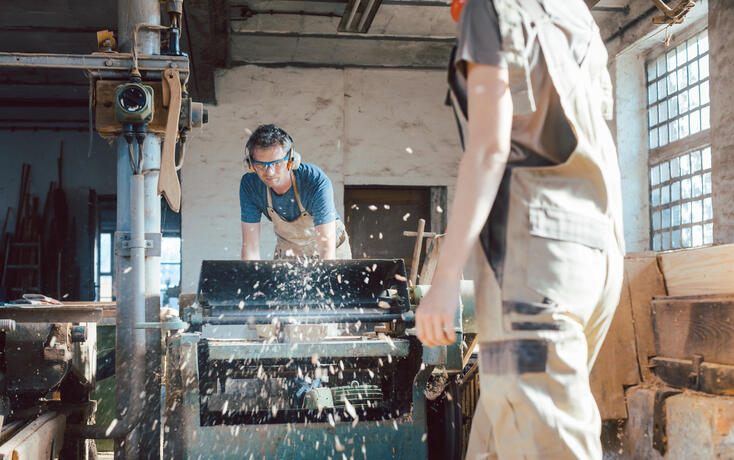 Team of carpenters planning wood using a machine