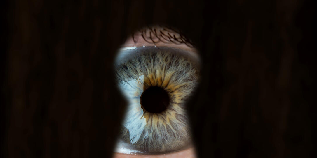 Female blue eye looking through the keyhole. Concept of voyeurism, curiosity, Stalker, surveillance and security