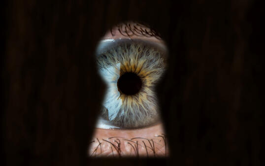 Female blue eye looking through the keyhole. Concept of voyeurism, curiosity, Stalker, surveillance and security