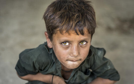 closeup of a poor staring hungry orphan boy in a refugee camp with sad expression on his face and his face and clothes are dirty and his eyes are full of pain