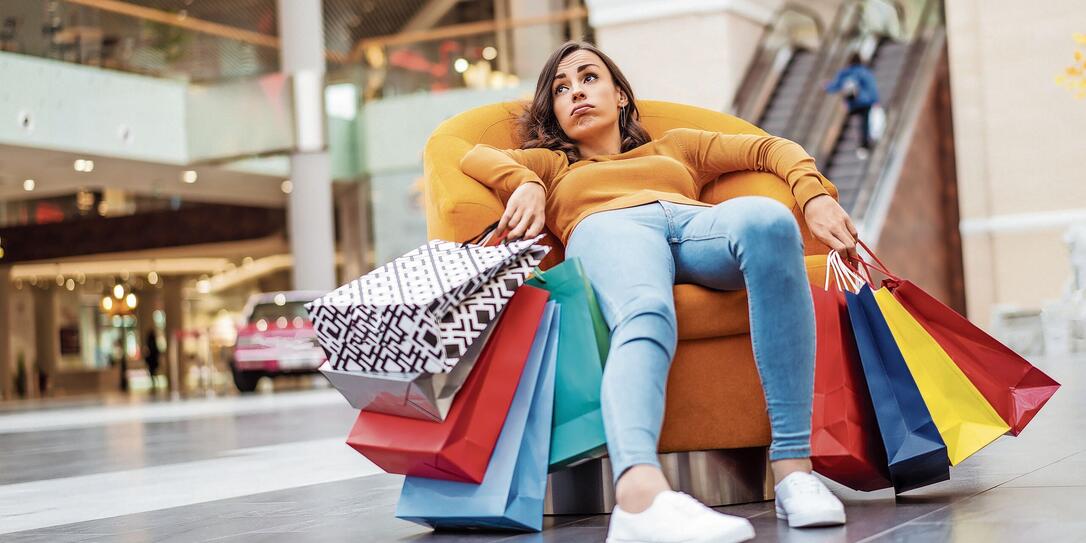 Tired and stressed young woman is lying and resting in the chair  with many shopping bags in the mall