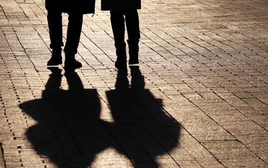 Two women walking down the street, silhouettes and shadows on pavement