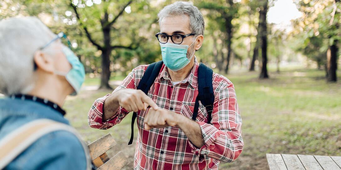 Senior man and his wife with protective face masks resting in the nature and talking on sign language Senior man and his wife with protective face masks resting in the nature and talking on sign language