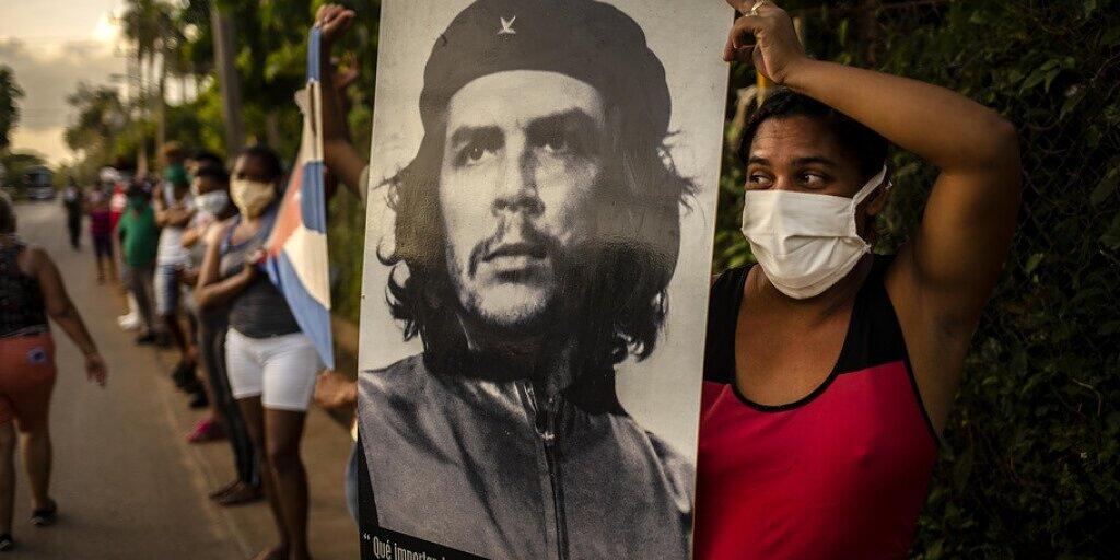 Frau in Havanna wartet während der Corona-Krise auf die Mediziner-Brigade des Henry Reeve Contingent und hält dazu das ikonische Foto "Guerillero Heroico" von Che Guevara hoch, das offenbar für jeden Anlass passt. Die Wohnung, in der Che geboren wurde, wird Fans zum Verkauf angeboten. (Archivbild)