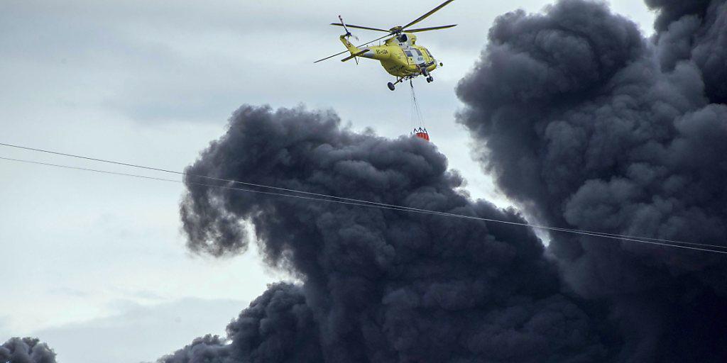 Ein Helikopter versucht das Feuer einzudämmen. Die brennenden Autoreifen verursachen eine Giftwolke. Ein Helikopter versucht das Feuer einzudämmen. Die brennenden Autoreifen verursachen eine Giftwolke.