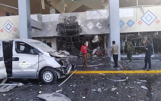 Menschen stehen in der Nähe eines beschädigten Gebäudeteils des Flughafens nach einer Explosion. Die Explosion traf das Flughafengebäude. Foto: Majid Saleh/AP/dpa