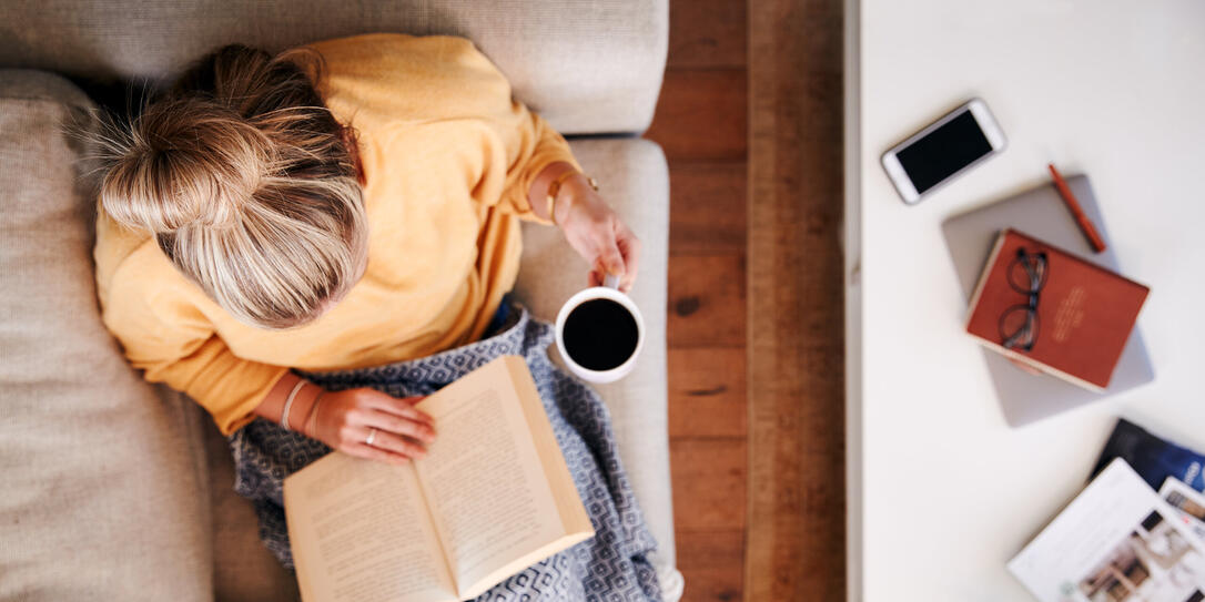 Overhead Shot Looking Down On Woman At Home Lying On Reading Book And Drinking Coffee Overhead Shot Looking Down On Woman At Home Lying On Reading Book And Drinking Coffee