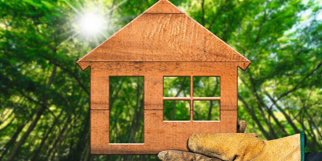 Hand with Work Glove Holding Holding a Small Wooden House in a Forest Hand with Work Glove Holding Holding a Small Wooden House in a Forest