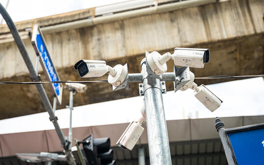 Close-up of a security street surveillance cameras on a pole under concrete Skytrain lines. Urban safety of citizens in the city