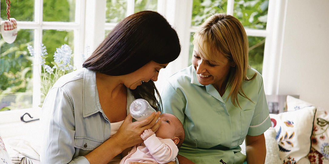 Mother bottle feeding a baby and meeting with health advisor