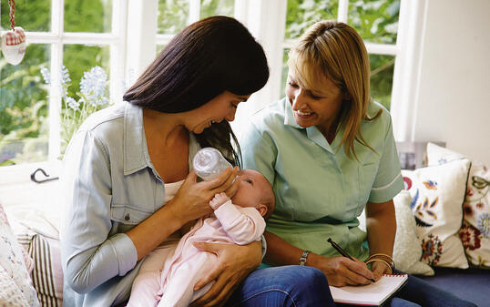 Mother bottle feeding a baby and meeting with health advisor