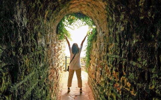 Silhouette of a lady with raised hands at the end of a tunnel