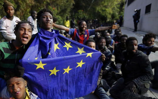 Einer der Flüchtlinge, die am Freitag erfolgreich den Grenzzaun bei Ceuta gestürmt hatten, hält eine EU-Flagge in seinen Händen. Am Montag gelang es erneut Hunderten Flüchtlingen, die spanische Exklave in Marokko zu erreichen. (Archiv)