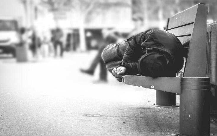 Poor homeless man or refugee sleeping on the wooden bench on the urban street in the city, social documentary concept, selective focus, black and white