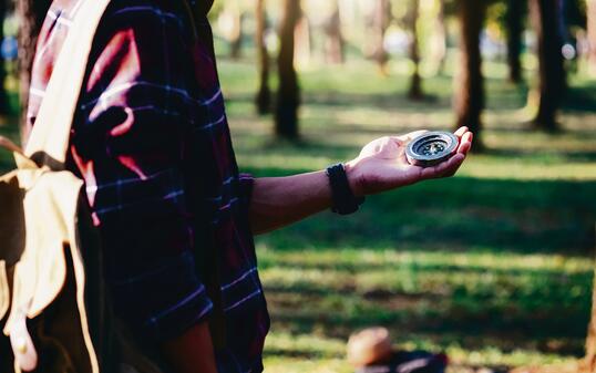 Hiker searching direction with a compass in the forest.