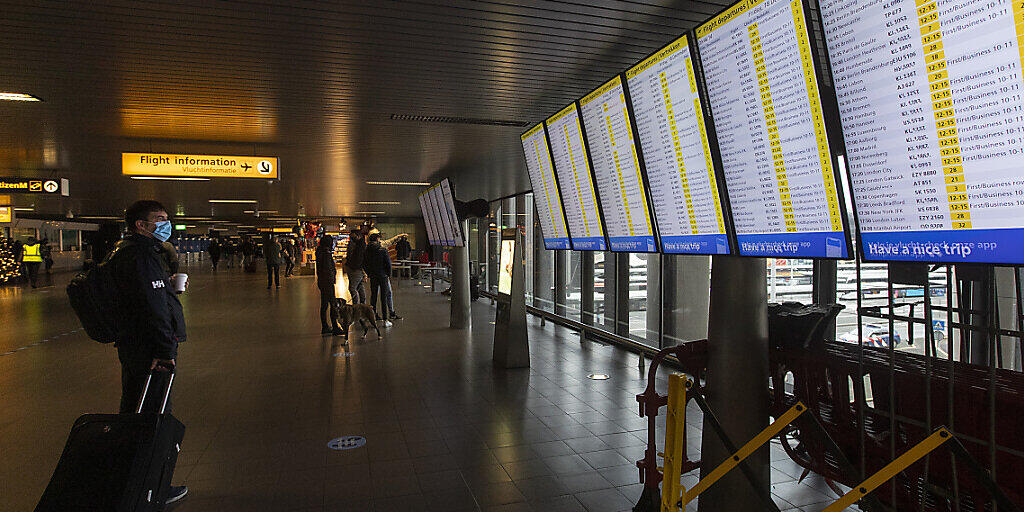 Ein Reisender, der als vorbeugende Maßnahme gegen die Verbreitung des Coronavirus eine Mund-Nasen-bedeckung trägt, schaut auf die Anzeigetafeln mit den Abflügen am Flughafen Schiphol bei Amsterdam. Foto: Peter Dejong/AP/dpa
