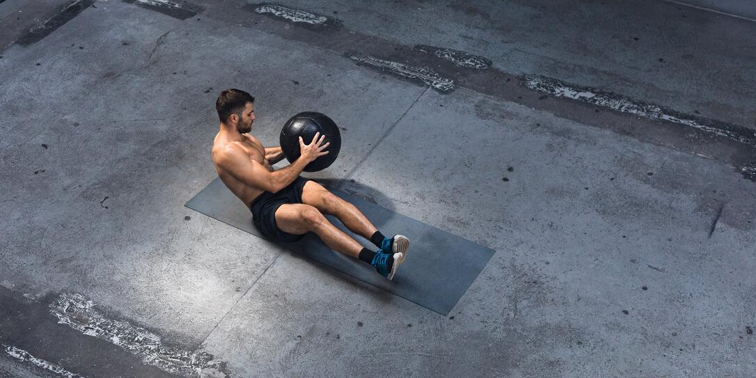 Fit Young Man Exercising Indoors - Doing Ab Exercises with a Medicine Ball