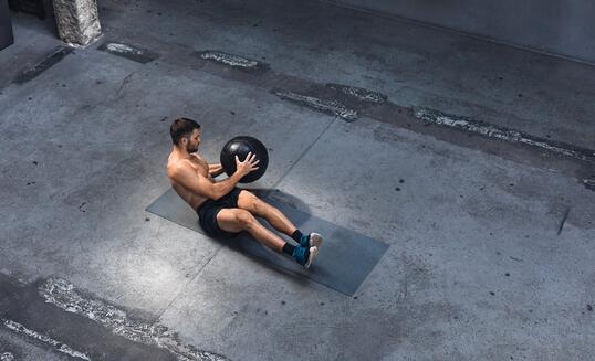 Fit Young Man Exercising Indoors - Doing Ab Exercises with a Medicine Ball