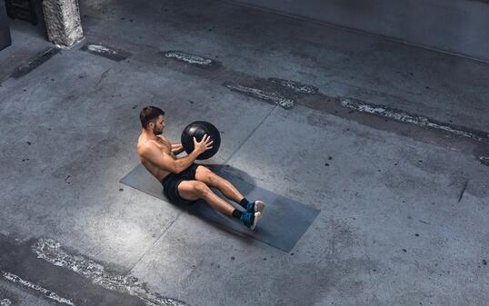 Fit Young Man Exercising Indoors - Doing Ab Exercises with a Medicine Ball