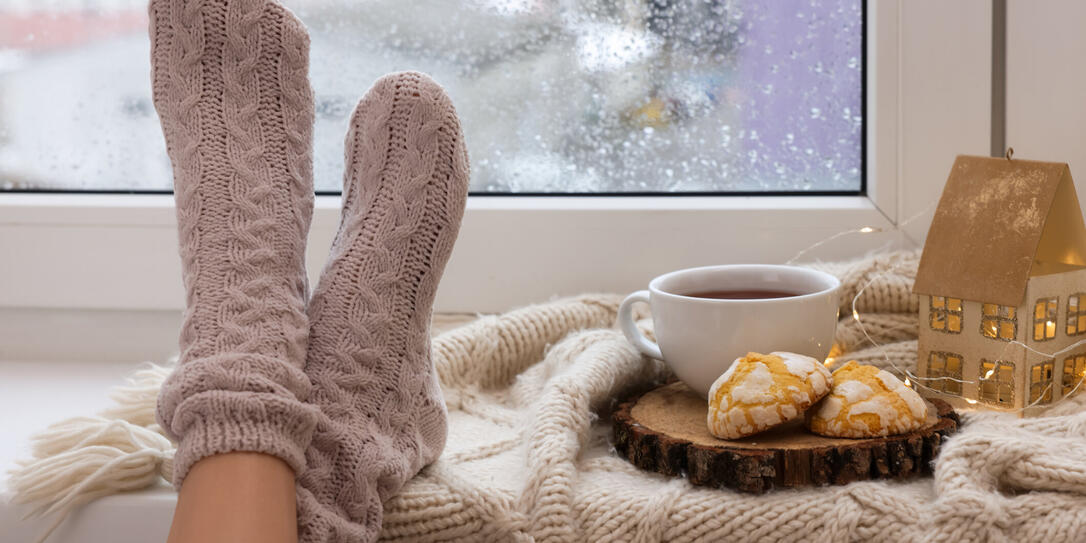 Woman in knitted socks relaxing near window at home, closeup. Space for text