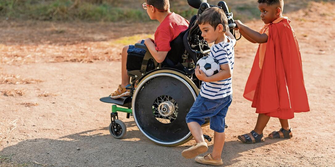 Diverse kids playing outdoors with wheelchair and soccer ball