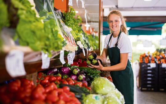 Young girl who works part-time as a trainee saleswoman puts on the showcase eggplants