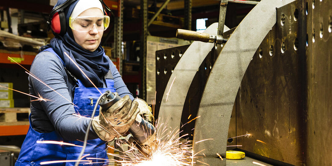 Young female trainee works with a grinder in a workshop, flying sparks