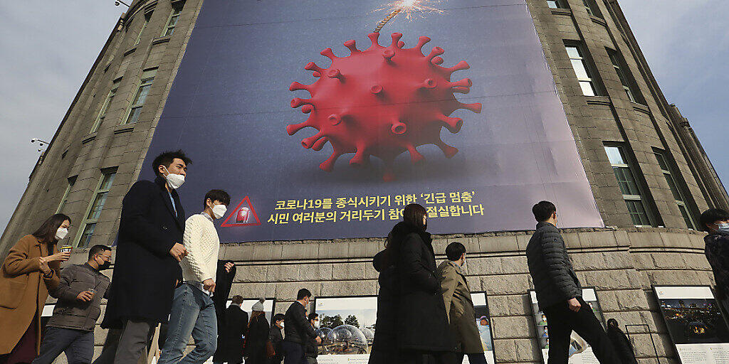 Menschen, die Gesichtsmasken tragen, gehen vor dem Rathaus von Seoul unter einem Transparent, das auf eine verstärkte soziale Distanzierungskampagne hinweist vorbei. Foto: Ahn Young-Joon/AP/dpa
