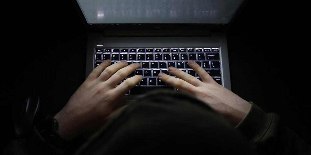 Person with a hoody typing at a computer in the dark. Suspicious online behavior