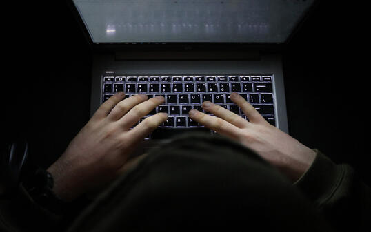 Person with a hoody typing at a computer in the dark. Suspicious online behavior