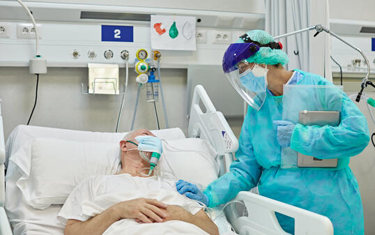 Female Doctor Supporting Male Patient Lying in Hospital Bed