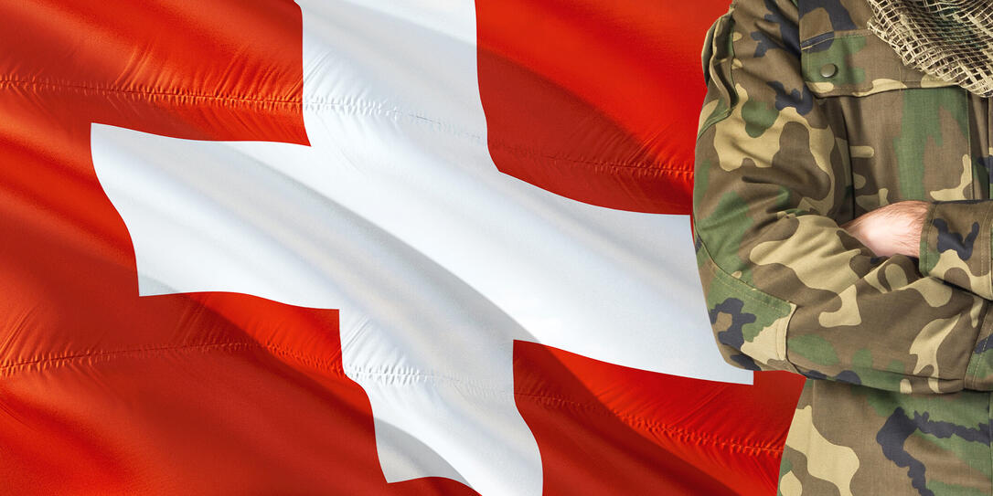 Crossed arms Swiss soldier with national waving flag on background - Switzerland Military theme.
